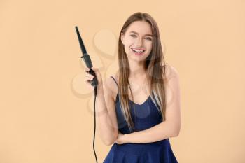 Young woman with curling iron on color background�