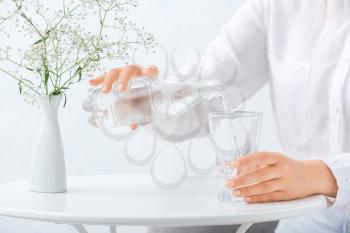Woman pouring water from bottle into glass on table, closeup�