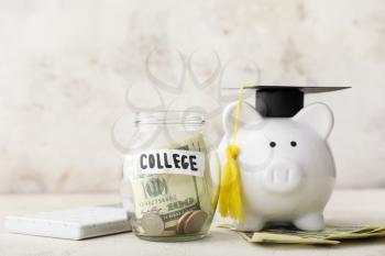 Piggy bank with graduation hat and jar with money for education on table. Tuition fees concept�