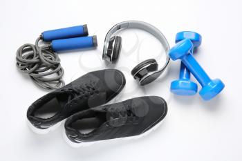 Sportive shoes, dumbbells, jumping rope and headphones on white background�