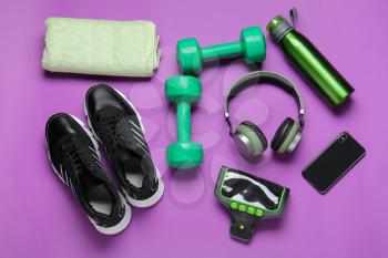 Bottle of water, dumbbells, sportive shoes and headphones on color background�