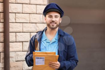 Handsome young postman with letters outdoors�