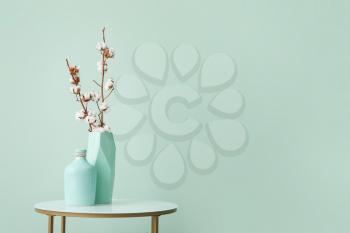 Vases with cotton flowers on stylish table near color wall in room�