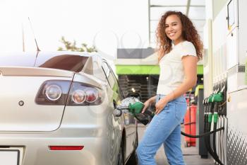 African-American woman filling up car tank at gas station�