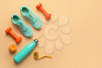 Dumbbells with shoes, bottle for water and measuring tape on color background�