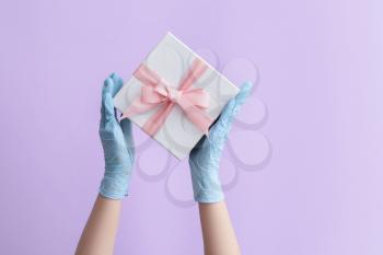 Hands in protective gloves and with gift box on color background�