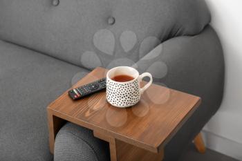 Cup of tea with remote control on armrest table in room�