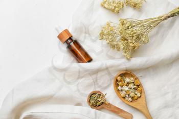 Composition with different herbs and bottle of essential oil on light background�