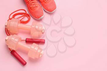 Dumbbells, sport shoes and skipping rope on color background�