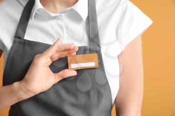 Young female waiter with blank badge on color background 