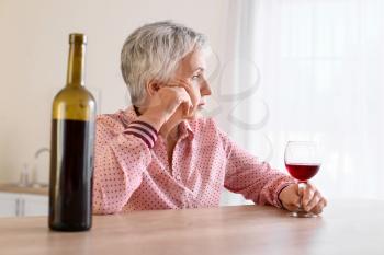 Stressed senior woman drinking wine at home�