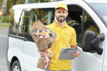 Delivery man with bouquet of beautiful flowers near car outdoors�