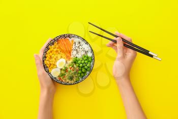 Woman eating tasty rice poke bowl on color background�