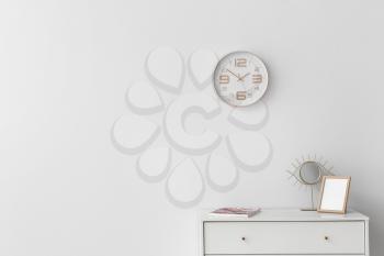 Blank photo frame, mirror and magazine on table against light wall with clock in room�