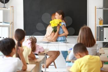 Little schoolgirl greeting her teacher in classroom�
