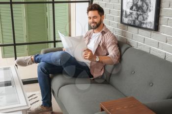 Young man reading magazine at home�