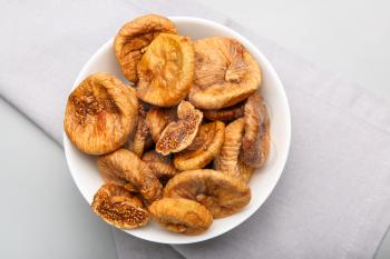 Bowl with tasty dried figs on light background�