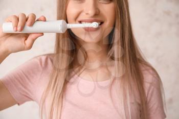 Young woman with electric tooth brush on light background�