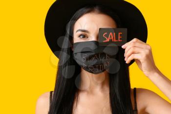 Beautiful young woman in medical mask and with credit card on color background. Black Friday sale�