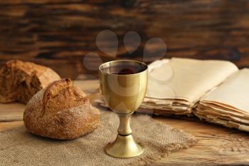 Chalice of wine with bread and Holy Bible on wooden background�
