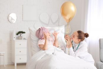 Doctor with golden balloon and little girl undergoing course of chemotherapy in clinic. Childhood cancer awareness concept�