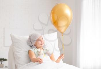 Little girl with golden balloon undergoing course of chemotherapy in clinic. Childhood cancer awareness concept�
