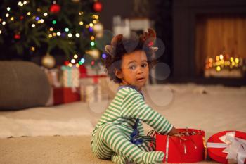 Cute African-American baby girl with gift at home on Christmas eve�