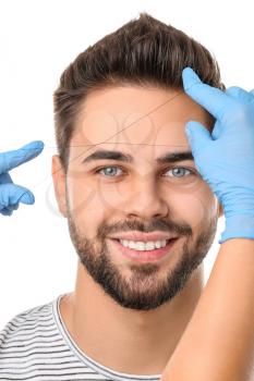 Young man undergoing eyebrow correction procedure on white background�