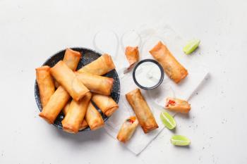 Plate with tasty fried spring rolls and sauce on light background�