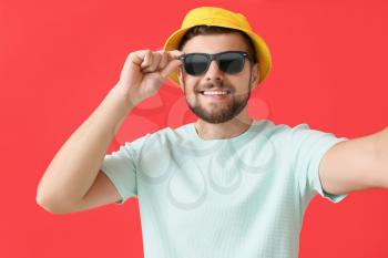 Handsome man with stylish sunglasses taking selfie on color background�