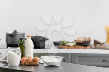 Bowl with flour, eggs and bottle of milk on table in modern kitchen�