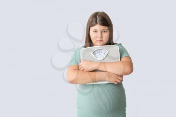 Sad overweight girl with measuring scales on light background�
