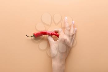 Female hand with chili pepper on color background. Erotic concept�