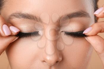 Beautiful young woman applying fake eyelashes, closeup�