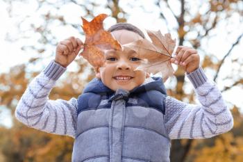 Cute African-American boy playing with leaves in autumn park�