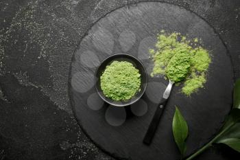 Bowl with powdered matcha tea and spoon on dark background�
