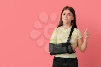 Young woman with broken arm showing thumb-up on color background�