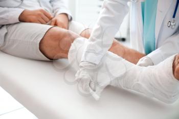 Doctor putting broken leg of young man in plaster�