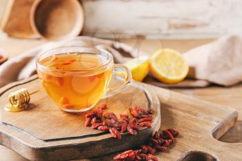 Glass cup of hot tea with goji berries on light wooden background�