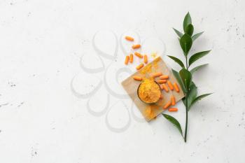 Turmeric pills and bowl with powder on light background�