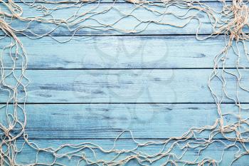 Frame made of fish net on color wooden background�