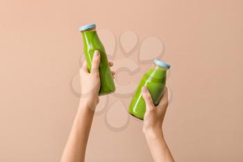 Woman holding bottles of healthy green smoothie on color background�