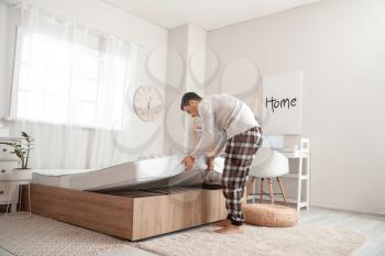Man putting soft orthopedic mattress on bed�