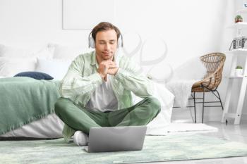 Handsome young man with laptop and headphones meditating at home�