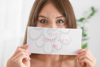 Beautiful young woman with gift voucher at home�