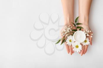 Female hands with cream and beautiful flowers on light background�