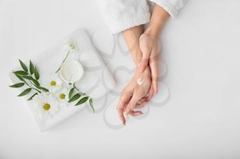 Female hands with cream, towel and beautiful flowers on light background�