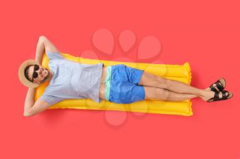 Handsome man lying on inflatable mattress against color background�