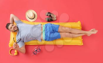 Handsome man lying on inflatable mattress against color background�