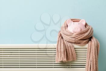 Piggy bank with scarf on radiator. Concept of heating season�